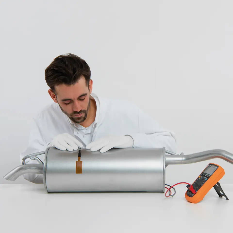 FHF06 high-temperature foil sensor measuring heat flux on a curved metal exhaust pipe.